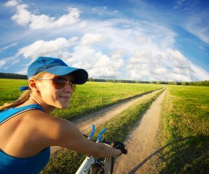19362672 - young smiling lady cycling on a countryside road at summer sunny day